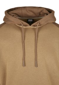 Rudas džemperis su kapišonu ir raišteliais. Audinys minkštas, kapišonas ir pečių sritis tamsesnės spalvos. Matoma prekės ženklo etiketė.