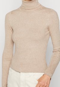 Vaaleanbeige, pehmeästä kankaasta valmistettu resorineuleinen pooloneule, jossa on vartalonmyötäinen leikkaus ja pitkät hihat, sekä teksturoitu pinta.