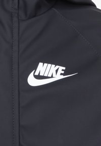 Čierna bunda Nike s hladkou textúrou, ktorá má výrazné biele logo na ľavej strane a bezproblémové švy.