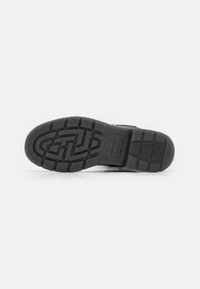 Semelle de chaussure en caoutchouc noir avec des motifs de semelle profonds et une surface texturée. Présente un logo circulaire et un design de rainure centrale pour une meilleure adhérence.