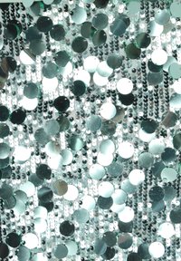 Tessuto argentato con paillettes e dischi riflettenti circolari, disposti in file verticali, creando una superficie testurizzata e scintillante.