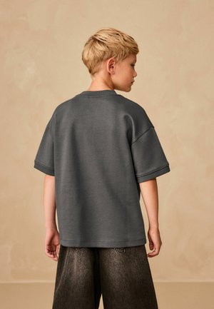 Sivý krátky rukávový sveter s okrúhlym výstrihom a uvoľneným strihom, skombinovaný s tmavými širokými nohavicami, z pohľadu zozadu. Hladká textúra.