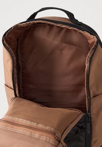 Šviesiai rudas kuprinės, kurios atvira pagrindinė dalis atskleidžia lygią vidinę apdailą ir priekinį užtrauktuką turintį tinklinį kišenę.