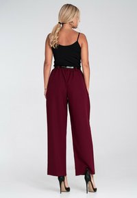Czarna bezrękawnikowa bluzka zestawiona z wysokogatunkowymi, bordowymi spodniami o szerokich nogawkach. Czarny pasek, czarne szpilki o spiczastym czubku, gładka tekstura materiału.
