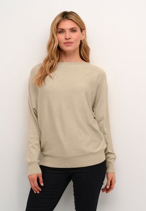 Pull beige à manches longues avec un col bateau et des poignets côtelés. Texture douce, coupe décontractée et silhouette légèrement allongée. Associé avec un pantalon noir.