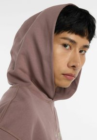 Sudadera con capucha en un malva suave, con costuras sin interrupciones y un acabado texturizado. La capucha cae sobre los hombros.