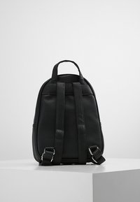 Svart läderryggsäck med texturerad yta, två justerbara axelremmar, litet handtag på toppen och minimalistisk design.