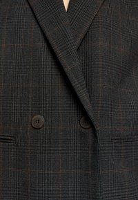 Blazer a cuadros en negro y gris con diseño de doble botonadura, adornado con botones marrones y una tela texturizada.