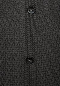 Grijze gebreide cardigan met een gestructureerde weefpatroon, twee zwarte knopen en een klassiek kraagontwerp. De stof lijkt zacht en warm.