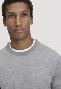 Grauer Sweater mit Rundhalsausschnitt, aus einem weichen, strukturierten Stoff gefertigt, mit einem weißen Innenkragen für einen Kontrast. Einfaches und modernes Design.