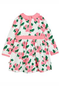 Långärmad klänning i vit bomull med rosa och gröna rosor, rosa krage och midjeband; har en knäppning med knappar bak.