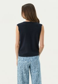 Marinblå ärmlös stickad topp med rund halsringning, kombinerad med ljusblå byxor med blommönster och vida ben. Mjuk textur och figurnära design.