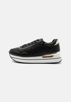 Czarny sneaker z białą podeszwą na platformie, złotym akcentem na pięcie i boku, tłoczonym okrągłym logo oraz czarnymi sznurówkami na białym tle.