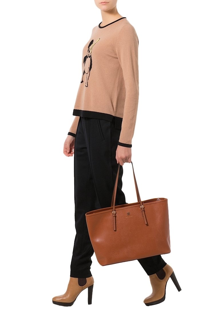 Femme portant un pull beige avec un motif graphique, un pantalon noir et des bottes à talons hauts couleur cuir clair, portant un grand sac cabas en cuir marron à ses côtés.