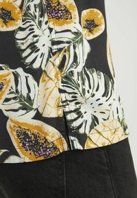 Schwarzer Stoff mit buntem Blumendesign, das gelbe Papayas und grüne Monstera-Blätter zeigt, strukturiert mit sichtbaren Stichen und Nahtdetails.