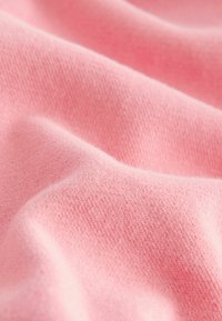 Ljust rosa stretchtyg med en mjuk textur, med en slät yta och subtilt stickat mönster som skapar mjuka veck och draperingar.