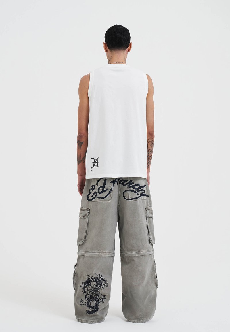 Witte mouwloze shirt en grijze cargo broek met zwarte geborduurde logo's en een draakontwerp. De broek heeft grote zakken en een relaxte pasvorm.