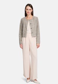 Checkered tweed jacket with round neckline and button closure, paired with wide-leg light beige trousers and pointed toe shoes.