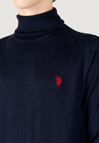 Maglione a collo alto navy realizzato in tessuto morbido, caratterizzato da un colletto a coste e da un piccolo logo rosso sul petto. Silhouette aderente.