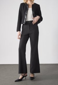 Black tailored jacket with a satin front panel, white top underneath, and black flared trousers. Match with black heeled slingback shoes.