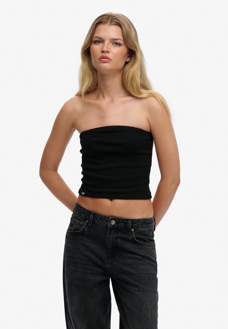 Top negro sin tirantes hecho de tela suave, con un diseño ajustado y un escote recto, combinado con jeans oscuros de cintura alta.