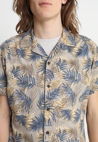Short-sleeved button-up shirt in light gray with blue, brown, and gold leaf patterns, featuring a collar and black buttons.