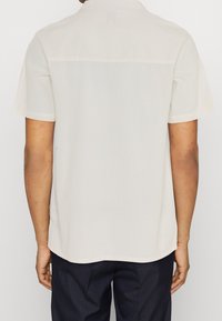 Korte mouwen, licht beige shirt met een subtiele ribbelstructuur, met een relaxte pasvorm en een rechte zoom, gezien vanaf de achterkant.