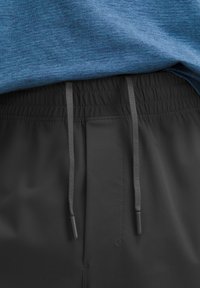 Sorte shorts med elastisk talje, der har en snor i matchende tone, parret med en struktureret blå sportsbluse.