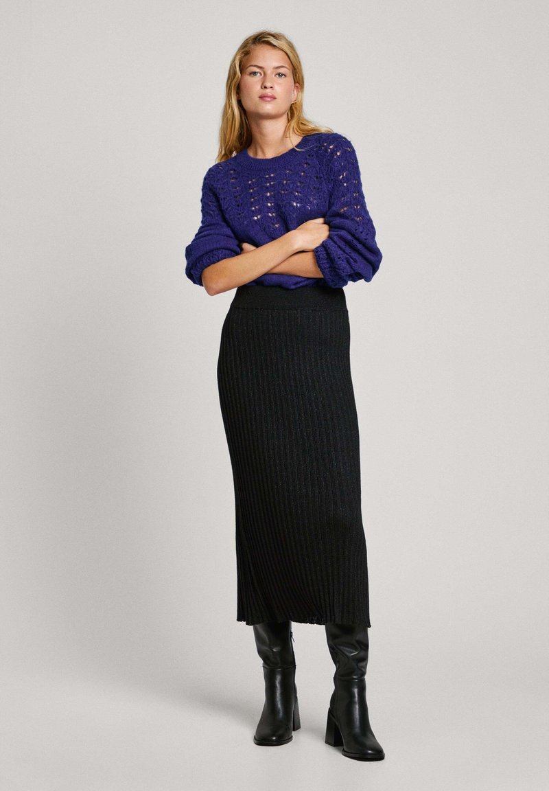 Suéter de punto morado con diseño de puntadas abiertas, combinado con una falda larga negra con trama acanalada y botas de tacón negras hasta la rodilla.