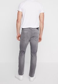 Szare dżinsy o slim fit, z tylnymi kieszeniami z dekoracyjnym przeszyciem, w połączeniu z białą koszulką z krótkim rękawem i białymi trampkami.