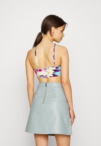 Top cropped com estampado floral e alças finas, apresentando um fecho nas costas. Combinado com uma saia mini de couro cinza claro de cintura alta.