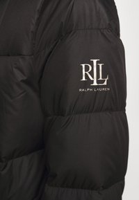 Svart puffjacka med kviltade sektioner, med en broderad silver "RLL" logotyp och "RALPH LAUREN" text på överarmen.