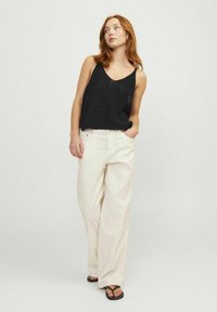 Top de tanque negro de punto con escote en V, combinado con pantalones de pierna ancha beige claro y chanclas negras. Fondo liso.