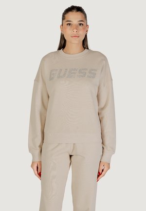 Felpa beige realizzata in morbido tessuto, con scollo rotondo, spalle scese e un logo scintillante "GUESS" sulla parte anteriore.