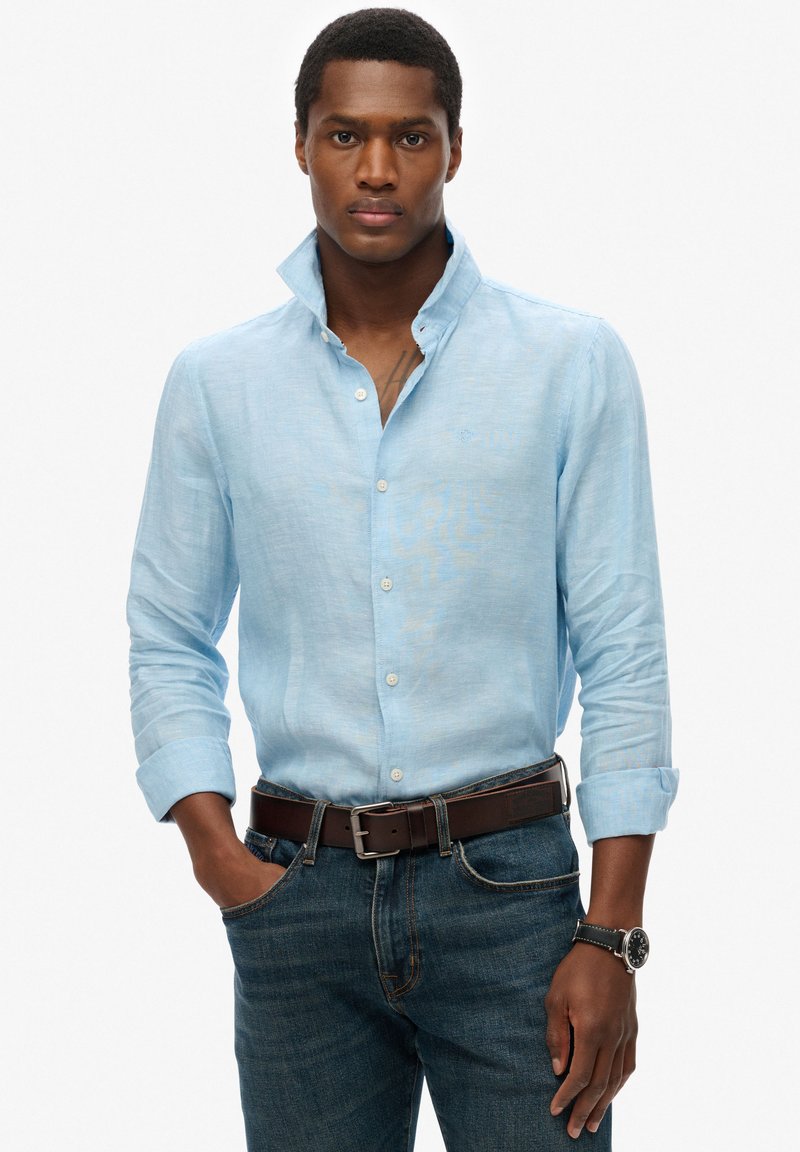 Lichtblauw linnen shirt met een button-down kraag, lange mouwen en een subtiele textuur. Gecombineerd met donkeren denim jeans en een bruine leren riem.