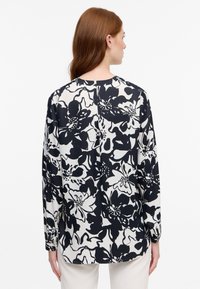 Blusa floreale in bianco e nero con maniche lunghe, scollo rotondo e vestibilità rilassata. Presenta un motivo floreale audace e una texture morbida.