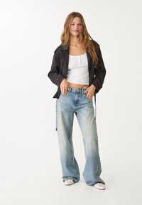 Svart jacka med skräddarsydd passform, vit croppad tanktop, ljusblå vida jeans och ljusa skor med dekorativa detaljer.