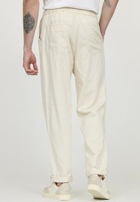 Heren crèmekleurige, relaxed-fit broeken met verticale strepen, elastische tailleband, zijzakken en opgerolde manchetten, gecombineerd met lichte sneakers.