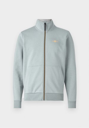 Jasnoniebieska rozpinana bluza z wysokim kołnierzem, przednimi kieszeniami, ściągaczami przy mankietach i dolnej części, z małym żółtym logo i gładką teksturą.