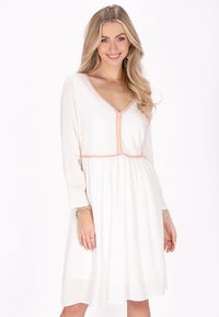 Rochie albă cu decolteu în V și mâneci lungi, cu accente brodate colorate de-a lungul gâtului și taliei. Material ușor și fluid.