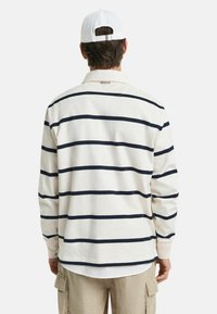 Lange mouwen polo shirt in crèmekleur met marineblauwe horizontale strepen, voorzien van een platte kraag en een lichtgebogen zoom. G gedragen met lichtbeige cargobroeken.