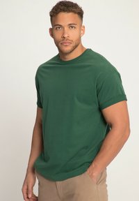 Camiseta verde de manga corta fabricada en algodón, con un escote redondo y puños de manga enrollados, exhibida en un modelo masculino.