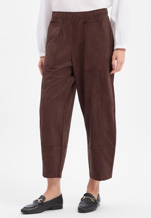 Bruine korte broek met elastische tailleband en grote zakken, gedragen met zwarte loafers en een wit tops met lange mouwen.