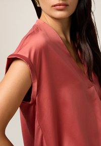 Blusa in satin color rosa, con scollatura a V, maniche corte arrotolate e un design semplice con linee pulite.