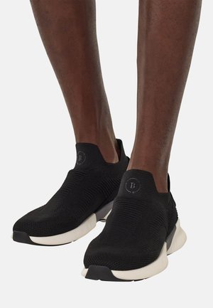 Sneakers neri slip-on con tomaia in maglia testurizzata, suola bianca e dettaglio del logo sul tallone. Forma sagomata per una vestibilità aderente.