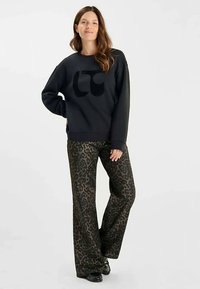 Sudadera negra con un gran logo negro en el pecho, combinada con pantalones de pierna ancha con estampado animal en tonos marrones y negros.