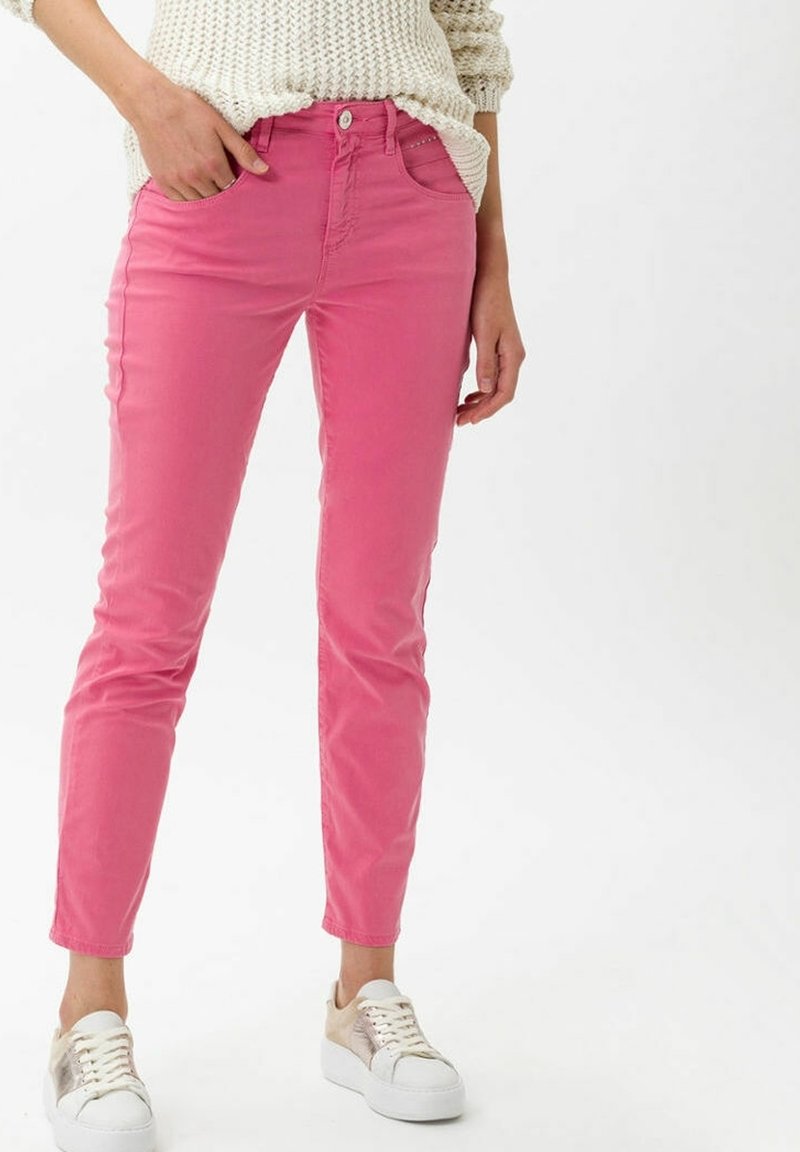 Jean skinny rose en denim avec une taille moyenne et des poches avant, associés à des baskets blanches avec une subtile touche métallique.