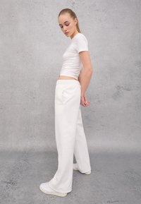 Witte top met korte mouwen gecombineerd met crèmekleurige wijdvallende sweatpants. De sweatpants hebben een elastische tailleband en zijzakken. Witte sneakers maken de look compleet.