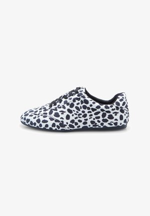 Weißer Sneaker mit schwarzen unregelmäßigen Punkten, schwarzen Schnürsenkeln und flacher Sohle, seitlich auf einem weißen Hintergrund dargestellt.