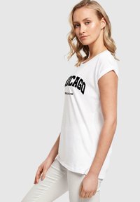 Witte katoenen t-shirt met opgerolde mouwen met "CHICAGO" in vette zwarte letters over de borst. Zachte textuur en een ontspannen pasvormontwerp.